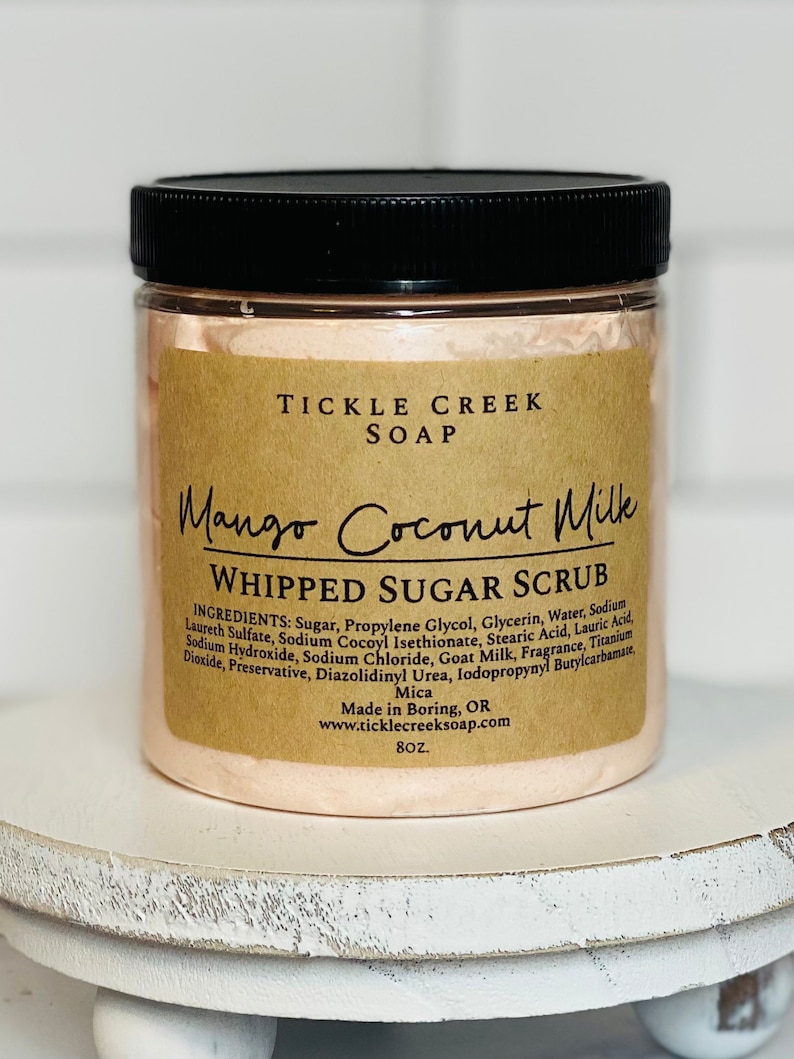May include: A pink whipped sugar scrub jar with a brown label that reads "Tickle Creek Soap Mango Coconut Milk Whipped Sugar Scrub". The label lists the ingredients and states "Made in Boring, OR" and "www.ticklecreeksoap.com". The jar is 8 oz.