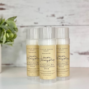 May include: Three white roll-on deodorant sticks with brown labels. The labels read "Tickle Creek Soap Handcrafted Lemon Eucalyptus All Natural Bug Deterrent Lotion Stick" and feature a handwritten font. Each stick is 2 oz.