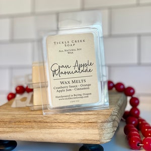 May include: A clear plastic container with a brown label that reads "Tickle Creek Soap, All Natural Soy Wax, Gran Apple Marmalade, Wax Melts, Cranberry Sauce - Orange, Apple Jam - Cinnamon, Handpoured in Boring, Oregon, www.ticklecreeksoap.com, 2.5 oz/72g".