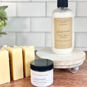 May include: Three bars of unscented goat milk soap and a small jar of unscented face lotion, both labelled "Tickle Creek Soap Handcrafted". The products are displayed on a white wooden pedestal.