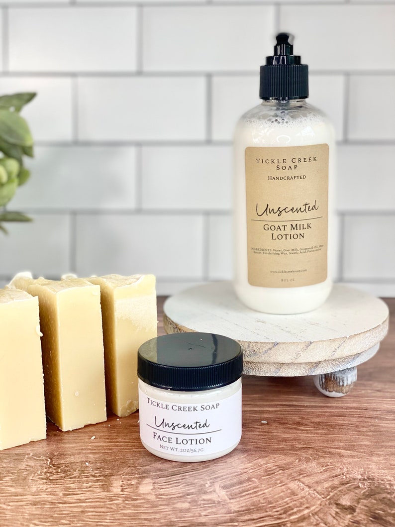 May include: Three bars of unscented goat milk soap and a small jar of unscented face lotion, both labelled "Tickle Creek Soap Handcrafted". The products are displayed on a white wooden pedestal.
