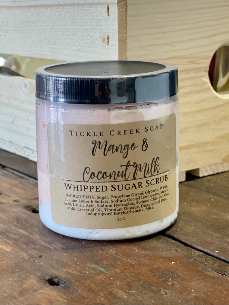 May include: A white jar with a brown label that reads "Tickle Creek Soap Mango & Coconut Milk Whipped Sugar Scrub". The label lists the ingredients and states the size is 8 oz.