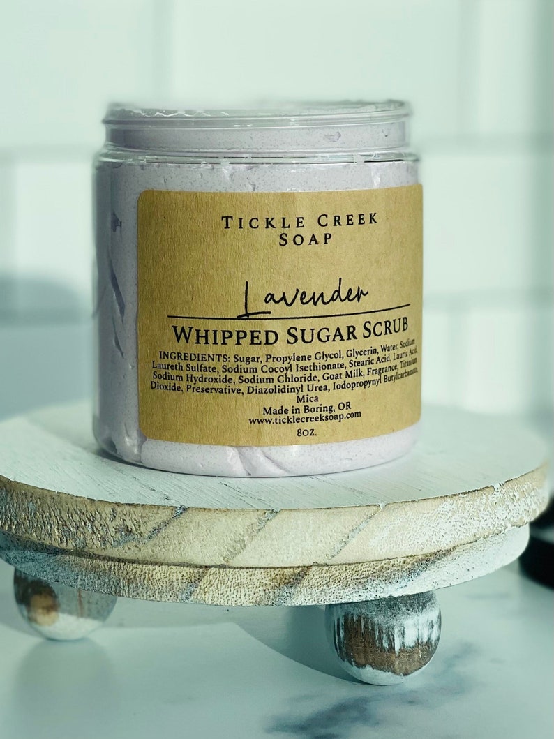 May include: A lavender-scented whipped sugar scrub in a clear jar with a brown label that reads "Tickle Creek Soap Lavender Whipped Sugar Scrub". The label lists the ingredients and states that the product is made in Boring, Oregon.