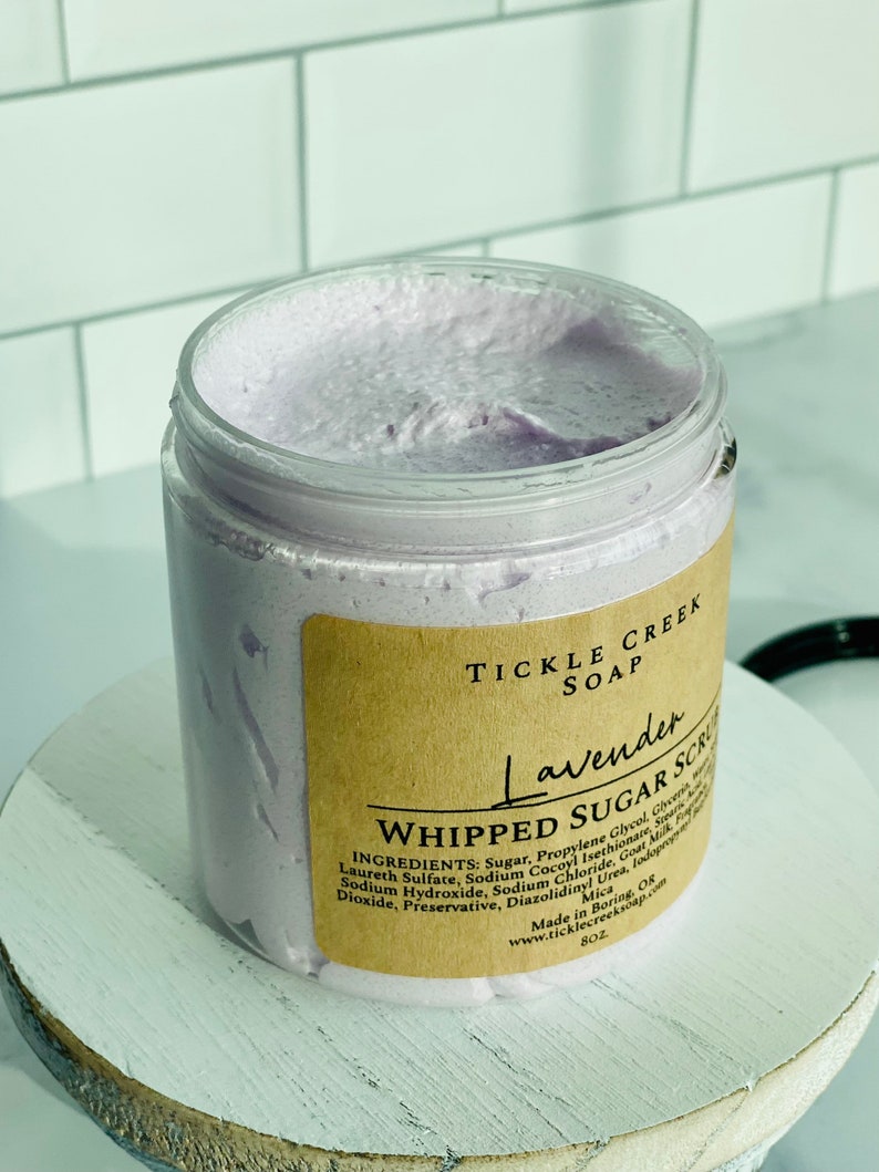 May include: A lavender-coloured whipped sugar scrub in a clear jar with a brown label that reads "Tickle Creek Soap Lavender Whipped Sugar Scrub". The label lists the ingredients: Sugar, Propylene Glycol, Glycerin, Laureth Sulfate, Sodium Cocoyl Isethionate, Sodium Hydroxide, Sodium Chloride, Goat Milk, Fragrance, Mica, Diazolidinyl Urea, Iodopropynyl Butylcarbamate, Preservative. Made in Boring, OK. www.ticklecreeksop.com 8 oz.