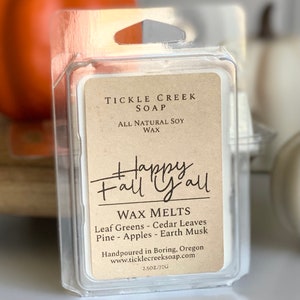 May include: A small clear plastic container with a brown label that reads "Tickle Creek Soap, All Natural Soy Wax, Happy Fall Y'all, Wax Melts, Leaf Greens - Cedar Leaves, Pine - Apples - Earth Musk, Handpoured in Boring, Oregon, www.ticklecreeksoap.com, 2.5 oz/70g".