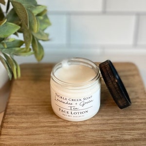 May include: A white jar of face lotion with a black lid. The label reads "Tickle Creek Soap Lavender + Green Tea Face Lotion Net Wt 2oz/56.7g".