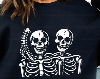 May include: A black sweatshirt with a white graphic of two skeletons holding hands. The skeletons are smiling and have a spine sticking out of one of their arms. The text "Digital Download | PNG |" is at the bottom of the graphic.