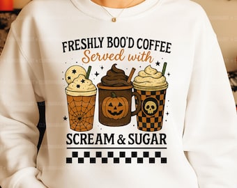 May include: White sweatshirt with a Halloween-themed graphic. The design features three coffee cups with whipped cream, a spiderweb, a pumpkin, and a skull. Text reads "FRESHLY BOO'D COFFEE Served with SCREAM & SUGAR."