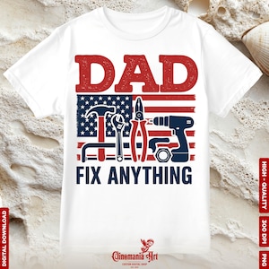 Puede incluir: Camiseta blanca con un diseño gráfico que presenta la palabra "DAD" en rojo sobre una bandera estadounidense estilizada con herramientas y el texto "FIX ANYTHING" en azul. El diseño incluye un martillo, una llave, unos alicates y un taladro.