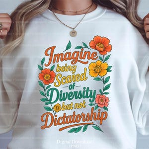 May include: White sweatshirt with the text "Imagine being Scared of Diversity but not Dictatorship" in orange, yellow, and green. The design includes floral accents in orange, yellow, and pink. Digital download.