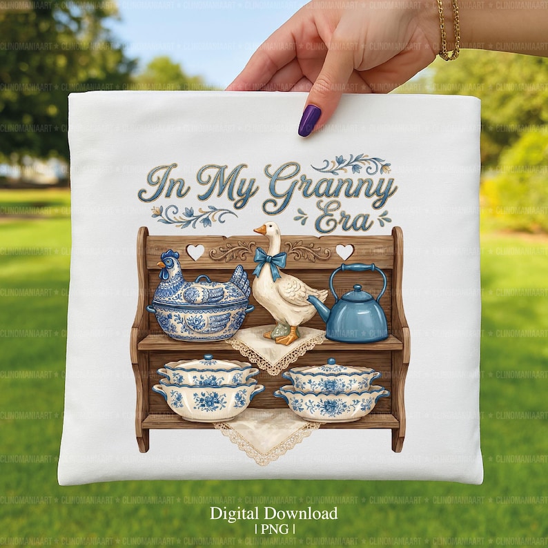 May include: White pillow with a vintage-style illustration. The design features a wooden shelf with blue and white ceramic dishes, a goose with a blue bow, and the text "In My Granny Era".