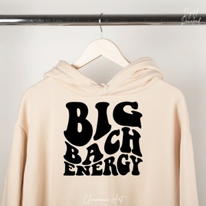 May include: A cream-coloured hoodie with a black graphic that says "BIG BACH ENERGY" in a retro font.