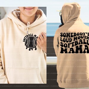 May include: Two beige hoodies with black text. One hoodie says "Softball Mama" with a baseball graphic. The other hoodie says "Somebody's Loud Mouth Softball Mama".