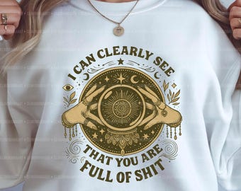 Op de afbeelding: Witte sweatshirt met een grafisch ontwerp met een kristallen bol die door twee handen wordt vastgehouden. Het ontwerp bevat de tekst "I CAN CLEARLY SEE THAT YOU ARE FULL OF SHIT". Het ontwerp is in goud- en bruintinten.