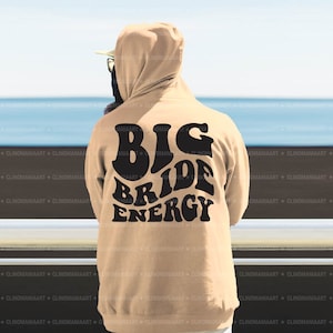 K&ouml;nnte beinhalten: Ein beiger Hoodie mit einem schwarzen Aufdruck auf der R&uuml;ckseite, der "Big Bride Energy" lautet.