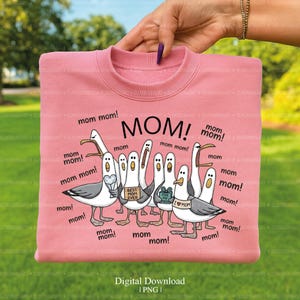 May include: A pink sweatshirt with the word "MOM!" in large black letters. The design features cartoon seagulls with "mom" speech bubbles. Some seagulls hold signs that say "Best Mom Ever" and "I love Mom".