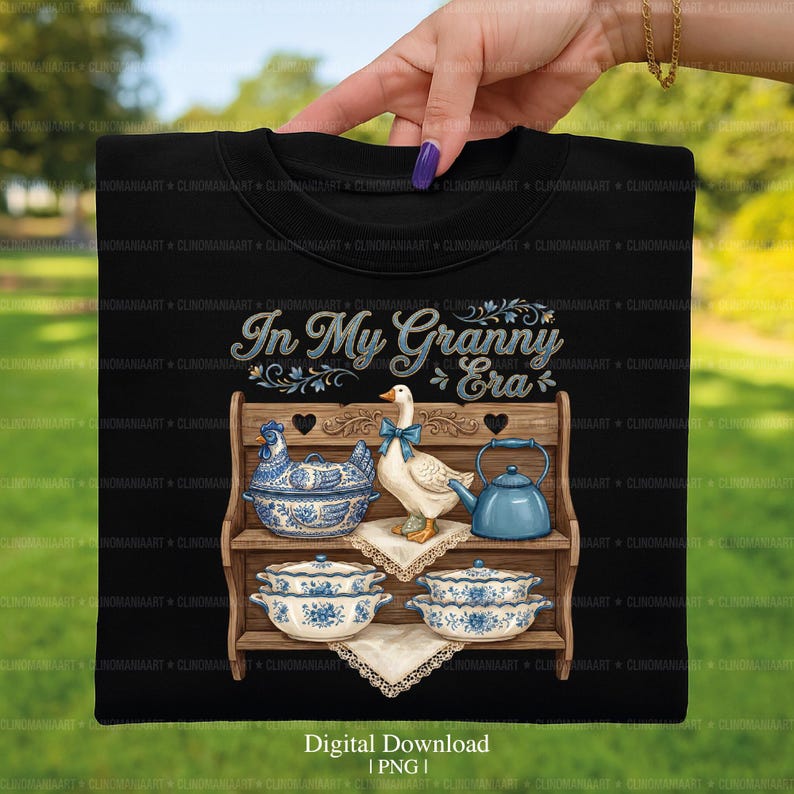 May include: Black t-shirt featuring a graphic of a wooden shelf with blue and white porcelain dishes, a goose with a blue bow, and a teapot. The text "In My Granny Era" is above the shelf. Digital download.