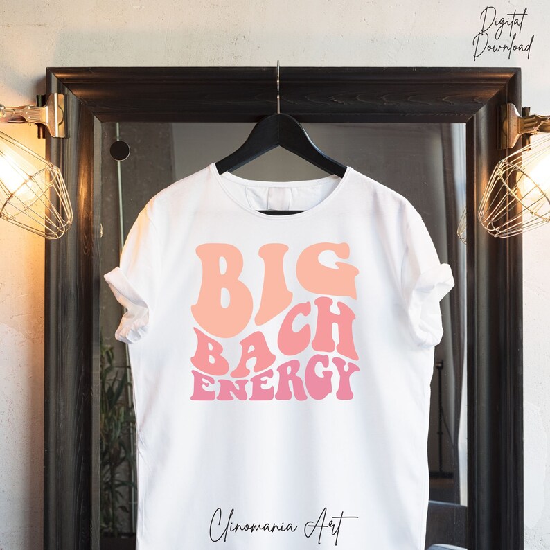 May include: White t-shirt with a pink and orange graphic that says "BIG BACH ENERGY" in a retro font.