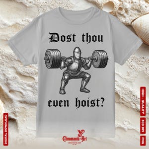 May include: A light gray t-shirt featuring a black and white illustration of a knight lifting a barbell. The text "Dost thou even hoist?" is above and below the illustration. The shirt has a crew neck.