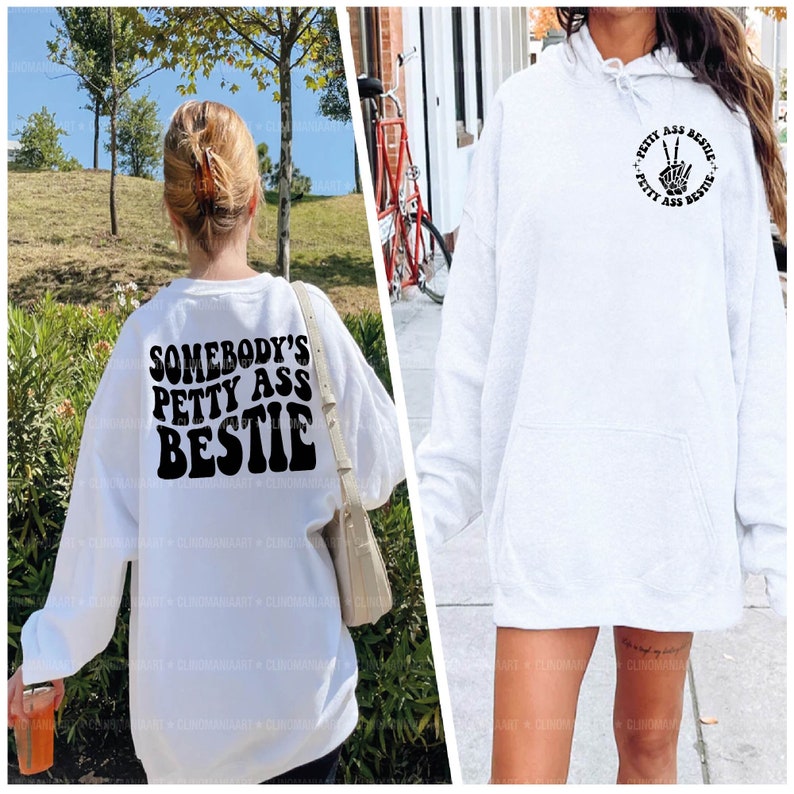 Op de afbeelding: Twee witte sweatshirts met zwarte tekst. E&eacute;n sweatshirt heeft de tekst "Somebody's Petty Ass Bestie" op de rug. De andere sweatshirt heeft de tekst "Petty Ass Bestie" in een cirkel met een vredesteken in het midden.