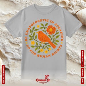 May include: A light gray t-shirt featuring a circular design with an orange bird, flowers, and the text "BE UNAPOLOGETIC IN SPEAKING UP FOR HUMAN RIGHTS." The design is surrounded by green leaves and yellow flowers. The shirt also has the text "DIGITAL DOWNLOAD" and "HIGH-QUALITY 300 DPI PNG."