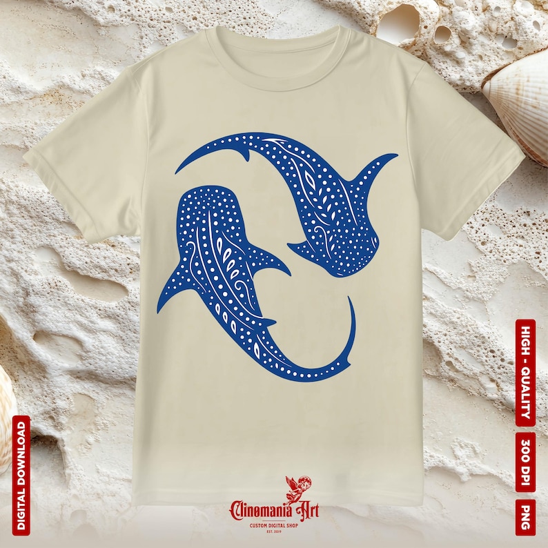 May include: A beige t-shirt featuring a blue graphic of two whale sharks swimming in a circle. The whale sharks have white spots and a white pattern on their bodies. The text "Cinomania Art" is printed on the bottom of the shirt.