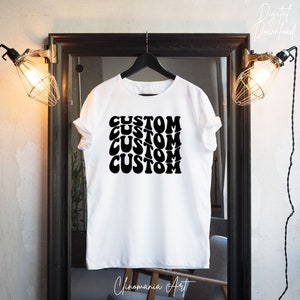 Puede incluir: Camiseta blanca con la palabra "CUSTOM" repetida cuatro veces en una fuente retro, negra y ondulada.