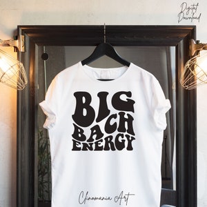May include: White t-shirt featuring a black graphic that reads "BIG BACH ENERGY" in a retro font.