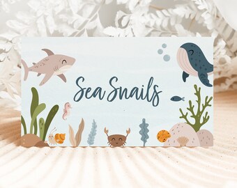 May include: A blue and white printable tag with a cartoon shark, whale, crab, seahorse, and seaweed. The text on the tag reads "Sea Snails".