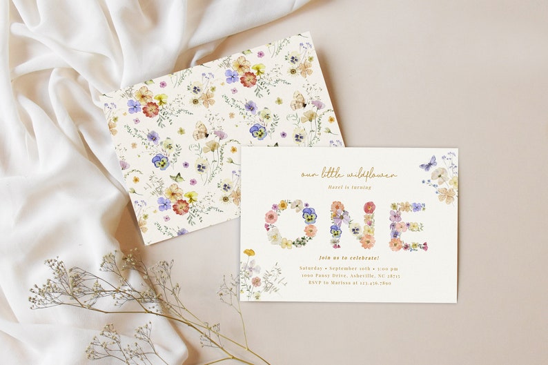 May include: A floral-themed first birthday party invitation with the word "ONE" spelled out in flowers. The invitation is decorated with a watercolor pattern of wildflowers and butterflies. The text reads "our little wildflower is turning ONE. Join us to celebrate! Saturday, September 10th, 4:00 pm 1000 Fancy Drive, Asheville, NC 28815 RSVP to Marion at 123-456-7890"