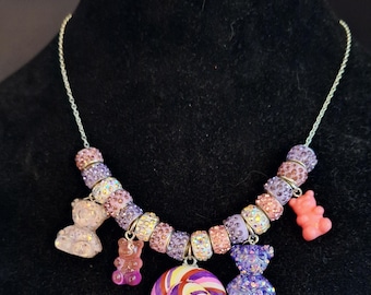 May include: A silver chain necklace with a variety of colorful charms, including gummy bears, a lollipop, and crystal beads. The charms are pink, purple, and clear.