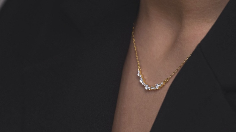 Puede incluir: Un collar de cadena de oro con una fila curva de peque&ntilde;as piedras preciosas transparentes.