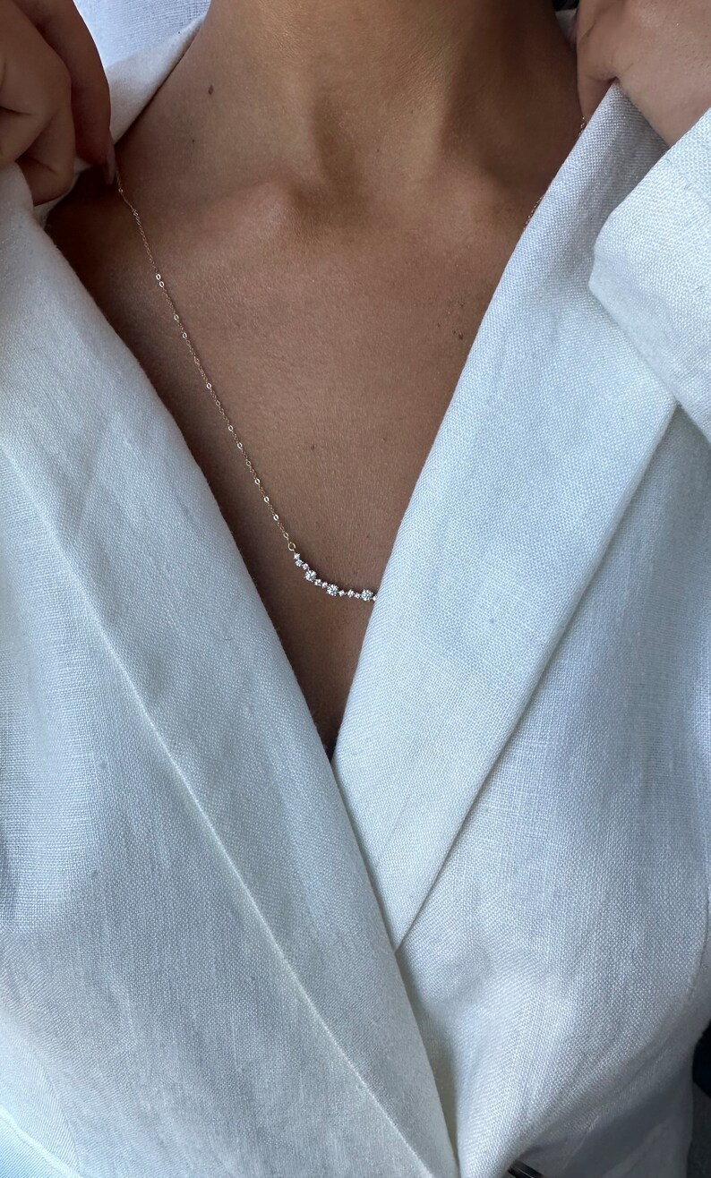 Puede incluir: Un delicado collar de oro con una fila de peque&ntilde;as piedras preciosas transparentes. El collar lo lleva una persona que lleva una chaqueta de lino blanca.