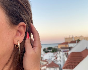 May include: Gold hoop earrings with a delicate chain dangling from one hoop.