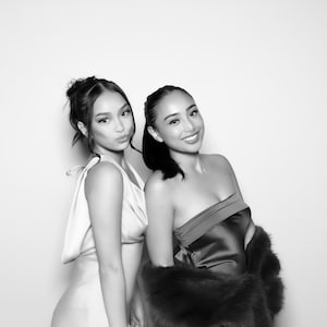 Puede incluir: Dos mujeres posando para una foto. La mujer de la izquierda lleva un vestido rosa claro sin mangas. La mujer de la derecha lleva un vestido negro sin tirantes con una estola de piel.