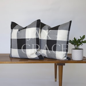 May include: Two black and white buffalo check throw pillows on a wooden bench.