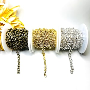 May include: Three spools of metal chain in antique bronze, gold, and silver tones. Each spool holds a continuous length of interlocking circular links, with a single strand of each chain extending downward from the center of the spool.