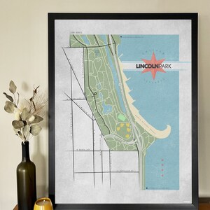 Może przedstawiać: Oprawiona grafika mapy Parku Lincolna w Chicago, z wystylizowaną ilustracją z zielonymi obszarami parku, niebieskim jeziorem i czerwoną gwiazdą z tekstem "Lincoln Park Illinois". Mapa jest w czarnej ramie.
