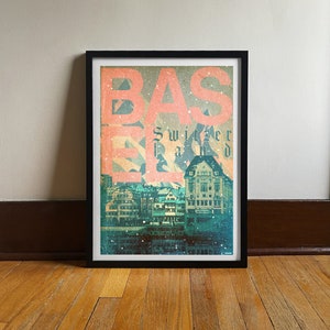 May include: A framed poster with a vintage aesthetic featuring the word "BASEL" in large, pink letters with a snowy background. The text "Switzerland" is written in smaller, white letters below the word "BASEL". The poster depicts a cityscape with buildings and a river.