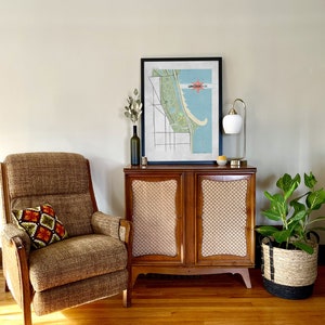 Może przedstawiać: Wnętrze salonu w stylu mid-century modern z brązowym fotelem, drewnianą szafką z siatkowymi panelami i oprawioną mapą Lincoln Park. Złota lampa i roślina doniczkowa dopełniają wystroju.