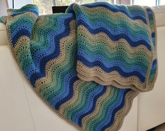 May include: A crocheted blanket with a wavy pattern in shades of blue, green, and brown. The blanket is draped over a white couch.