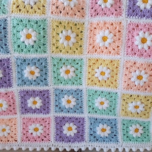 May include: A crocheted baby blanket with a daisy pattern in pastel colors. The blanket is made of soft yarn and has a white border.