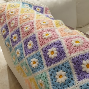 May include: A crocheted baby blanket with a pastel rainbow color scheme and a daisy flower pattern. The blanket is made with soft yarn and has a delicate white border.