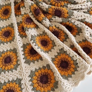 May include: A crocheted throw blanket with a sunflower pattern in shades of brown, yellow, and green.