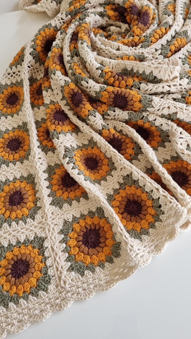 May include: A crocheted throw blanket with a sunflower pattern in shades of brown, yellow, and green.