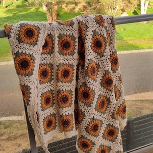 May include: A crocheted throw blanket with a sunflower pattern in shades of brown, yellow, and green. The blanket is draped over a railing.