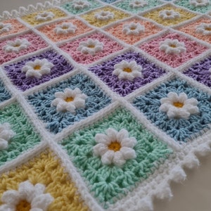 May include: A crocheted baby blanket with a white border and a daisy pattern in pastel colors, including yellow, green, blue, purple, pink, and orange.