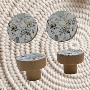 May include: Two round wooden knobs featuring a printed map illustration of the Hundred Acre Wood. The top surface of each knob displays black line drawings of characters and trees on a light background, while the base is natural wood.