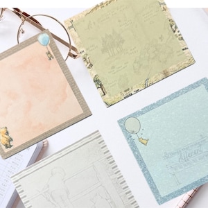 May include: Four square Winnie the Pooh themed sticky notes. One is peach with a Winnie the Pooh graphic, another is light green with a map design, a third is light blue with the word "Different", and the last is a sketch.