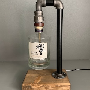 May include: A black metal pipe lamp with a wooden base. A clear glass bottle with a label that reads "HIBIKI Japanese Harmony" is suspended from the lamp.
